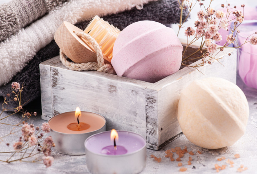 Bunte Badekugeln, kleine bunte Teelichter, zusammengelegte Handtücher und eine Bürste sorgfältig zusammengelegt und präsentiert als Geschenkset.