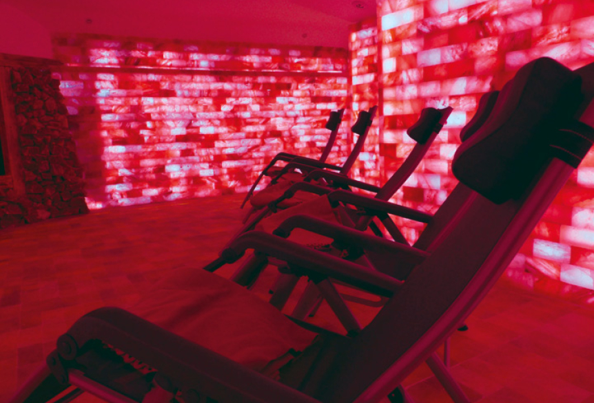 Mehrere Relaxliegen in einem Ruheraum mit roten Salzwänden, warmem rosa Licht und salzbedecktem Boden.