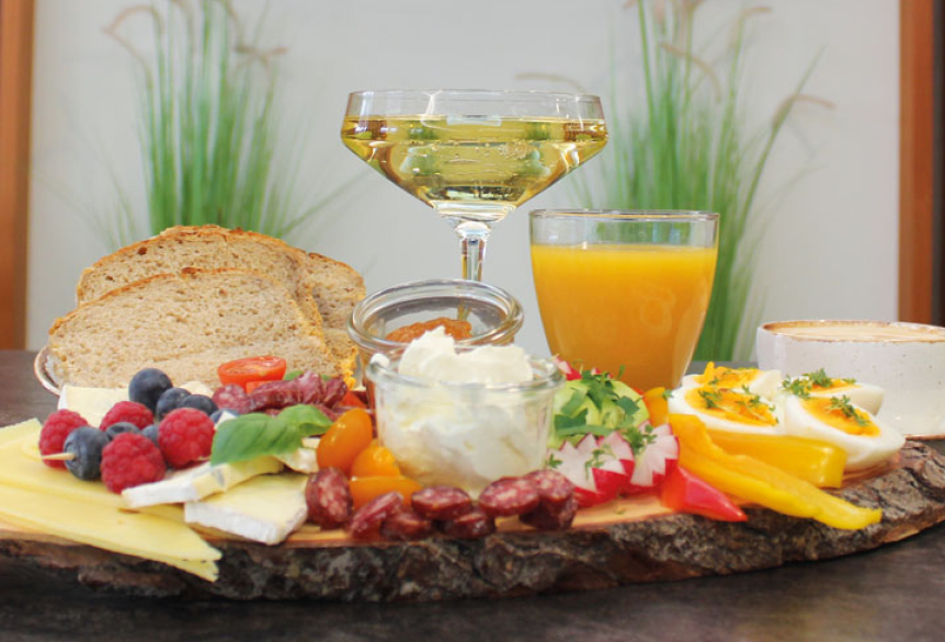 Auf einem Tisch steht ein leckeres Sektfrüstück mit frischem Obst, Käseschnitt, Brotscheiben, frischen Orangensaft, Kaffee und Sekt.