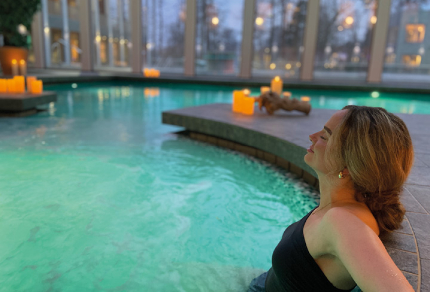 Eine Frau sitzt mit geschlossenen Augen entspannt in einem Whirlpool, umgeben von warmem, sprudelndem Wasser.