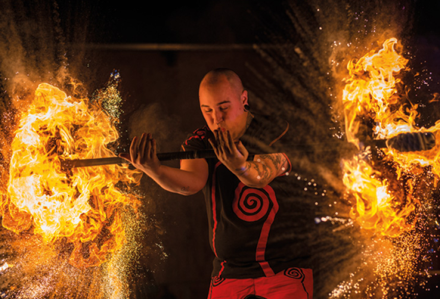 Ein Mann führt eine Feuershow vor und hält eine Feuerstange, deren beide Enden in Flammen brennen.