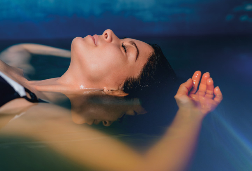 Eine Frau treibt mit geschlossenen Augen entspannt auf der Wasseroberfläche des AquaSound Beckens