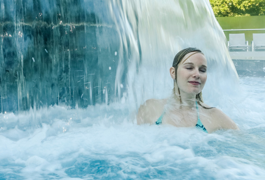 Frau steht unter einem Strömungspilz in der SaarowTherme, Wasser massiert ihre Schulter, sie schließt die Augen und genießt den entspannenden Moment.