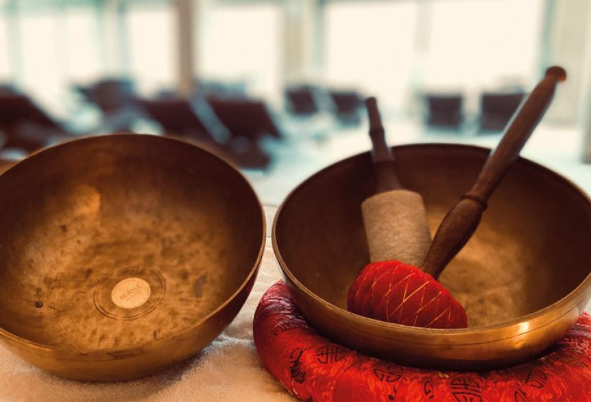 Zwei Klangschalen mit Klöppeln stehen auf einem Tisch, eine davon auf einem roten Kissen.