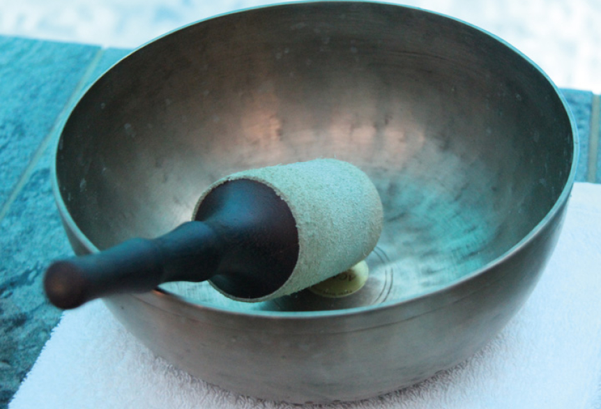 Mehrere Klangschalen liegen auf Tüchern, daneben ein Klöppel für die Klangmassage.