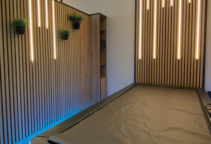 Raum mit Akkustikpanelen und warmen Lichtleisten, blaue Akzentbeleuchtung, Hydrojet-Massageliege mit LED Beleuchtung.