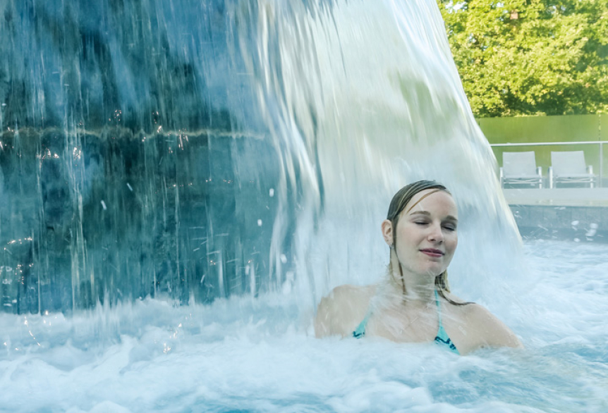Frau entspannt im Whirlpool unter Wasserfall im Freien, lächelnd