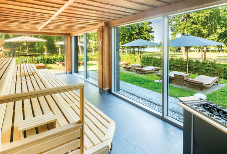 Moderne Sauna mit Blick durch Glasfront auf Kurpark mit Liegen und Sonnenschirmen