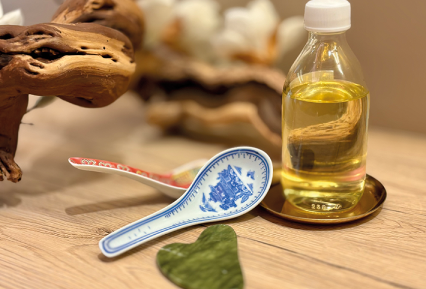 Flasche Massage-Öl und Gua Sha-Löffel auf Holztisch
