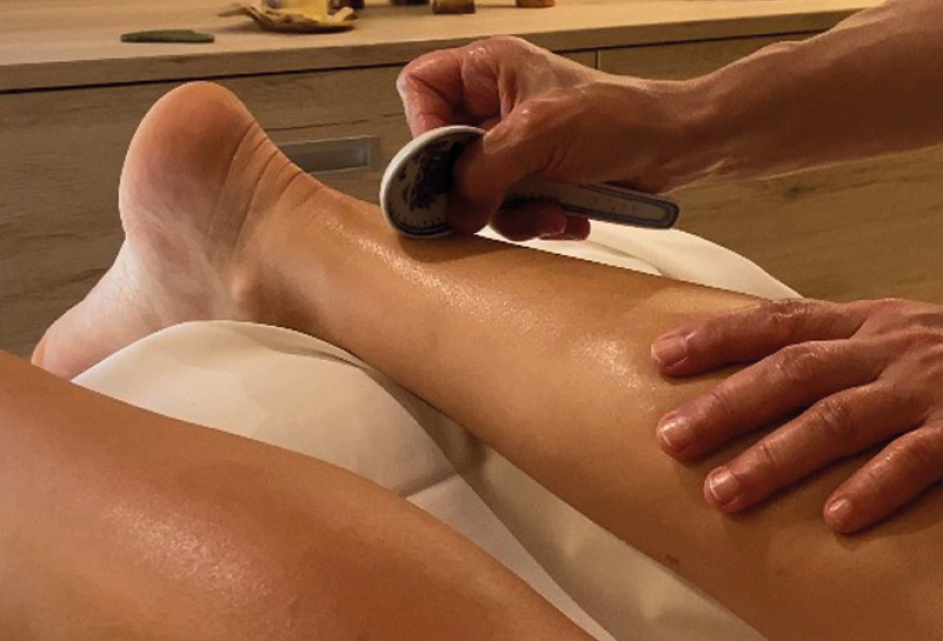 Gua Sha Massage am Bein; Hände streichen über Wade und Fuß