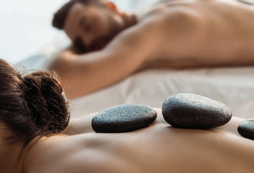 Ein Paar liegt entspannt nebeneinander bei einer Hot-Stone-Massage in ruhiger Atmosphäre.