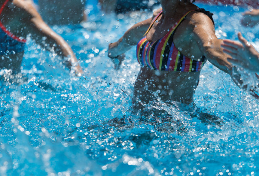 Mehrere Personen bewegen sich im Wasser eines Pools, Wasser spritzt.