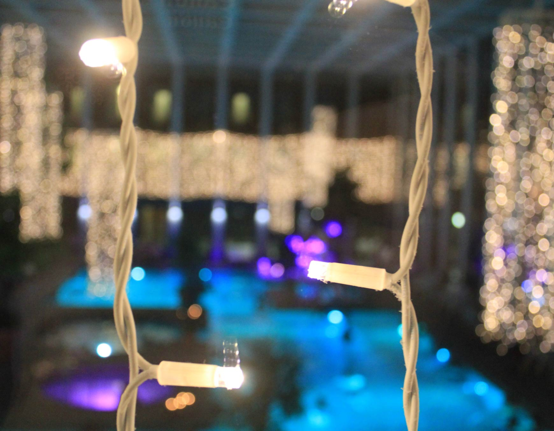 Das Innenbecken der SaarowTherme wird blau mit lila Farbtupfern beleuchtet und die warm-weißen Lichterketten, hängend von der Decke, ergeben eine gemütliche Atmosphäre am Abend. 