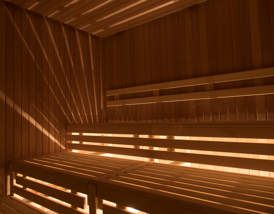 Innenansicht der stilvoll beleuchteten BioSauna mit hölzernen Sitzbänken auf mehreren Ebenen und indirektem Licht, das durch die Holzlatten strahlt und ein warmes Ambiente schafft.