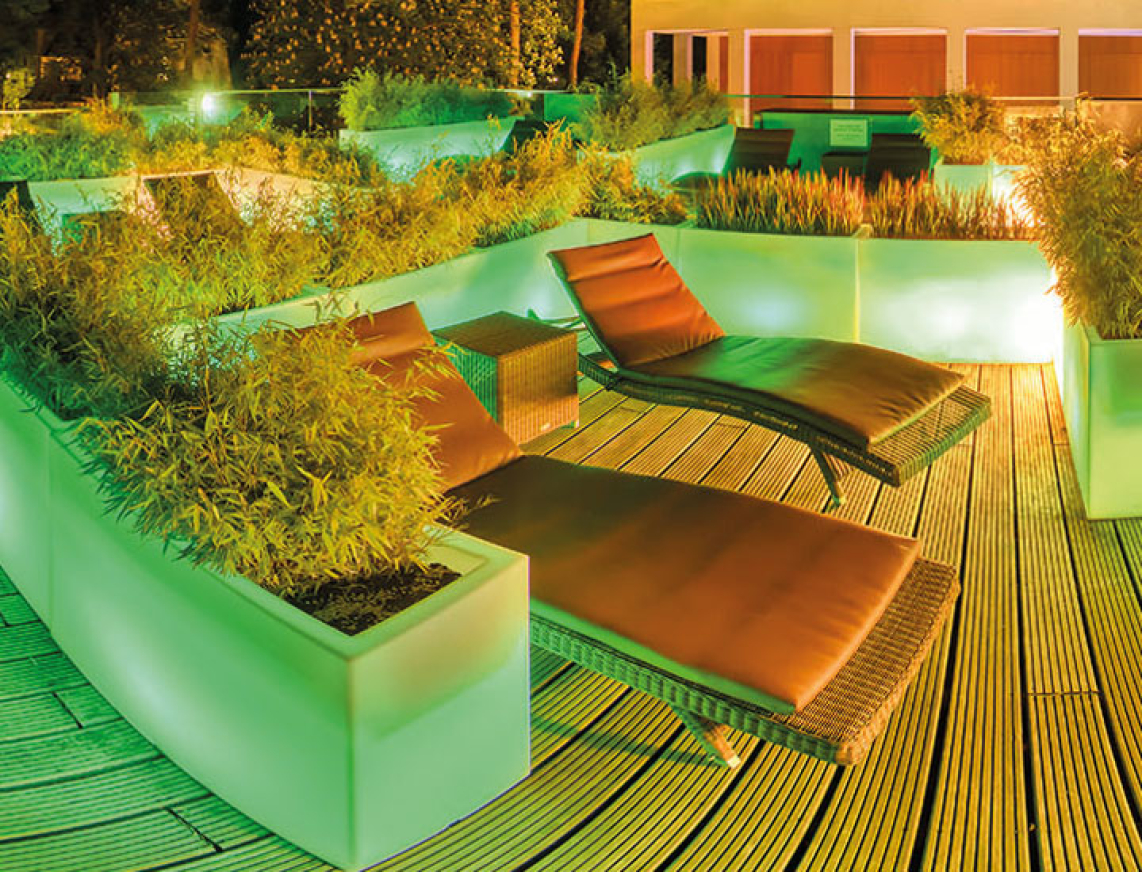 Weitläufige Dachterrase mit leuchtenden Planfkübel, die mit Gräßer bepflanzt sind. Kleine Relaxzonen sind mit Sonnenliegen bestückt und laden zum Verweilen ein.