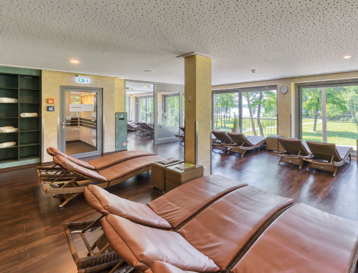 Moderner Ruhebereich mit ergonomischen, braunen Liegen auf zwei Ebenen. Große Fenster geben Ausblick auf den Kurpark von Bad Saarow.