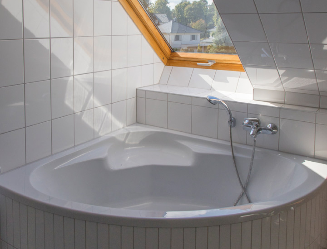 Große Badewanne direkt unter einem Dachfenster platziert in einem Badezimmer. Weiße Fliesen an den Wänden und Fußboden tauchen das Badezimmer in einem hellen und freundlichen Licht. 