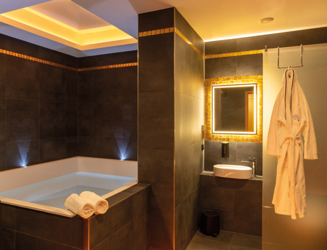 Modern gestaltender Floatingraum in SaarowTherme mit großer Floating-Wanne, beleuchtetem Spiegel über einem Waschbecken und einem aufgehängten Bademantel. Stimmungsvolle Lichtakzente schaffen eine entspannte Atmosphäre.
