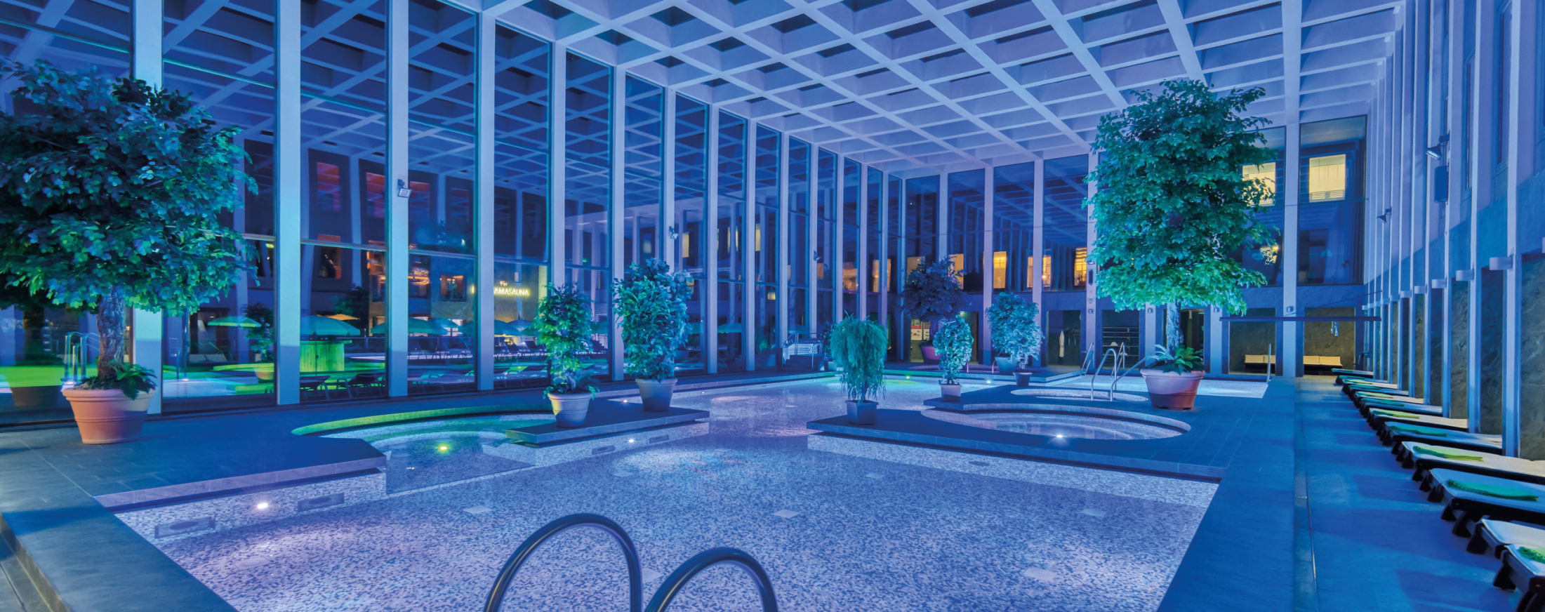 Das Thermalbad der SaarowTherme mit Abendbeleuchtung. Blau und grünes Licht und beleuchtete Becken tauchen das Thermalbad in einer romantischen Atmosphäre.