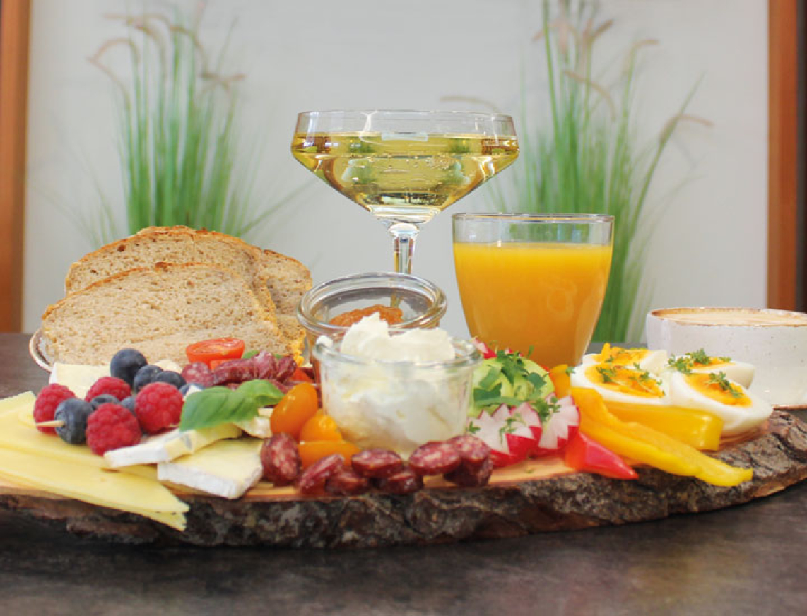 Auf einem Tisch steht ein leckeres Sektfrühstück mit frischem Obst, Käseschnitt, Brotscheiben, frischen Orangensaft, Kaffee und Sekt.