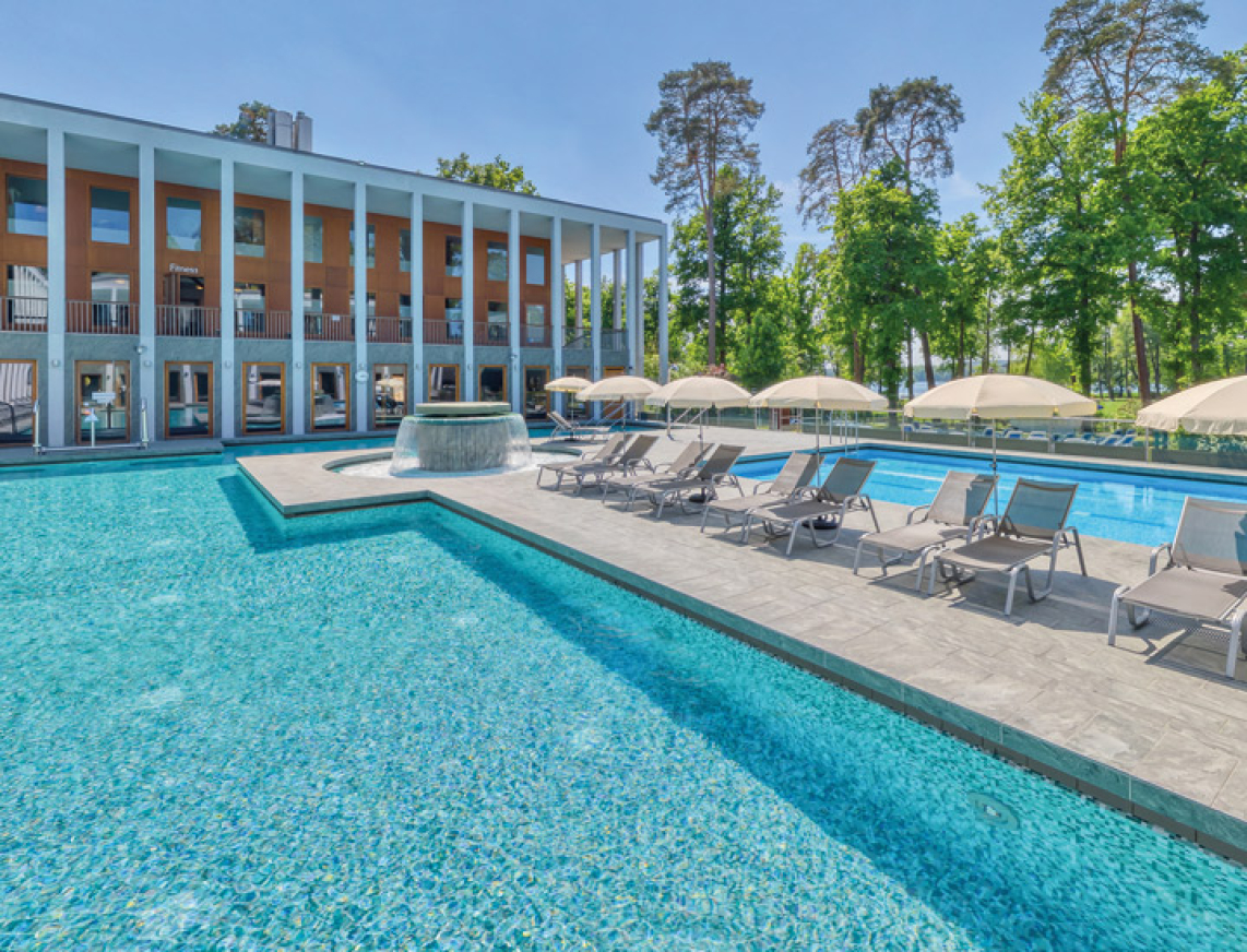Außenbereich der SaarowTherme mit Thermalsolebecken, Strömungskanal und Sonnenliegen. Entspannende Atmosphäre unter blauem Himmel.