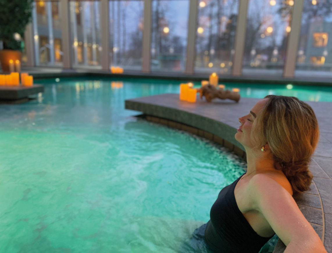 Eine Frau sitzt mit geschlossenen Augen entspannt in einem Whirlpool, umgeben von warmem, sprudelndem Wasser.