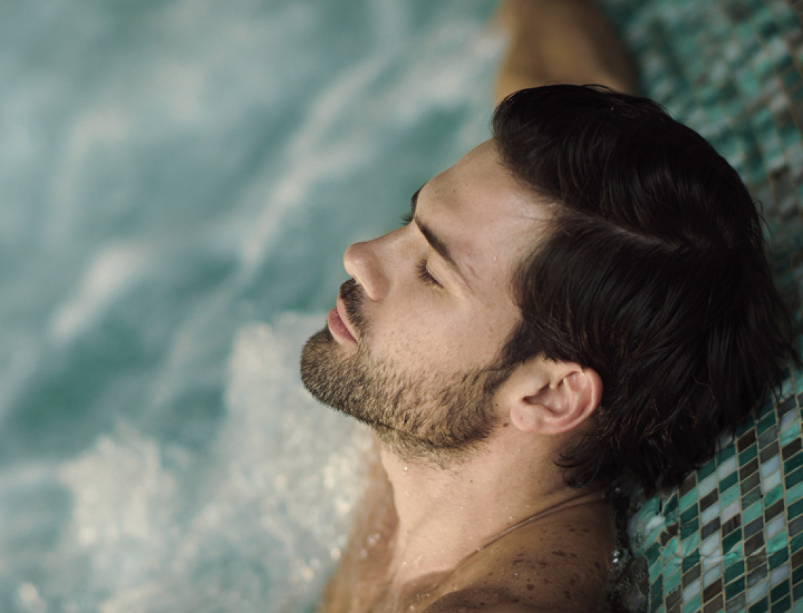 Mann sitzt entspannt im Whirlpool, lehnt sich zurück, hat die Augen geschlossen und genießt die warmen Sprudelbewegungen.