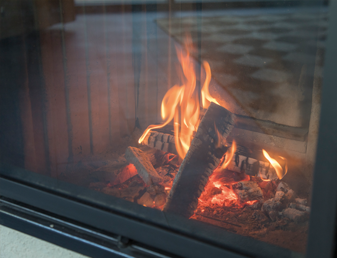 Loderndes Feuer mit Holzscheiten im Kamin hinter Glasscheibe.