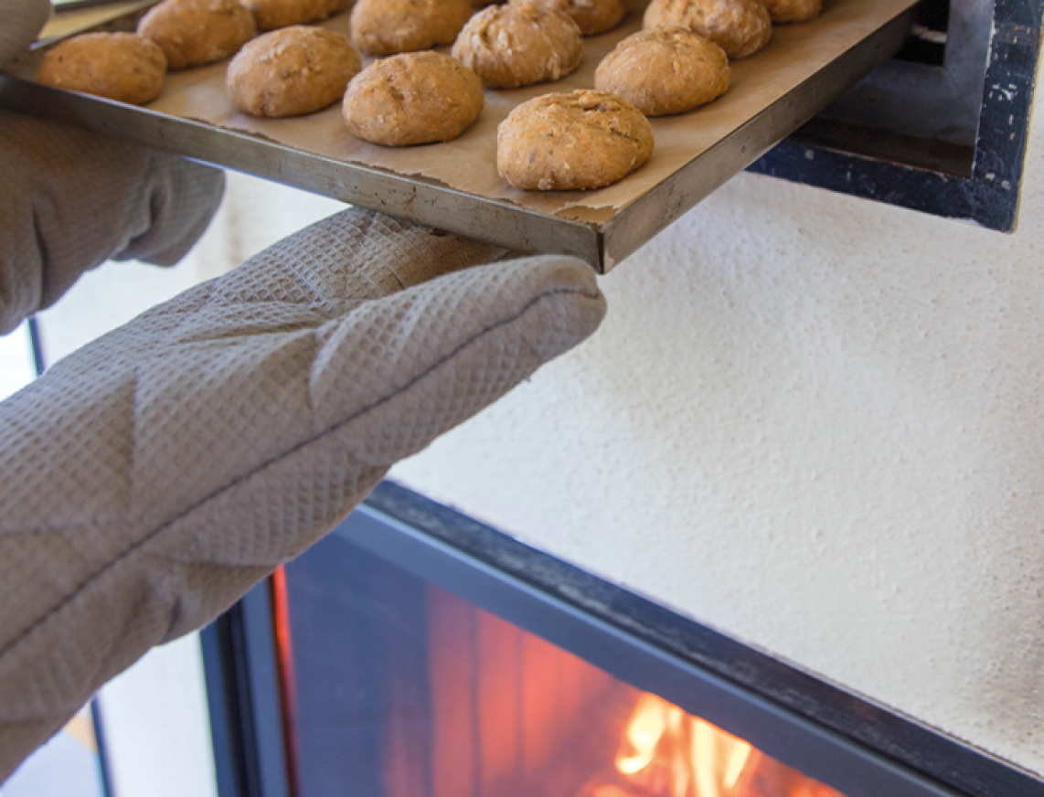 Hand im Ofenhandschuh schiebt Blech mit Brötchen in Ofen